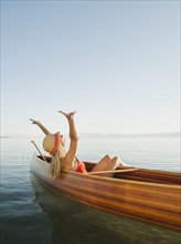 Young woman relaxing in canoe with arms raised.