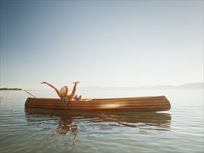 Young woman relaxing in canoe with arms raised.