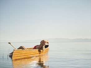 Young woman relaxing in canoe with arms raised.