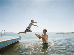 Boy (4-5) jumping into lake caught by his father.