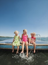 Girls (2-3, 4-5) sitting at the edge of raft and splashing water.