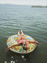 Girl (4-5) floating on water on inflatable ring and laughing.