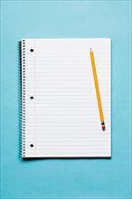 Single yellow sharpened pencil with blank spiral notebook on blue background. Photo : Kristin