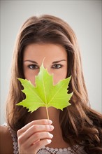 Beautiful woman holding green sycamore leaf in front of mouth and nose. Photo : Mike Kemp