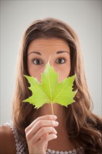 Beautiful woman holding green sycamore leaf in front of mouth and nose. Photo : Mike Kemp