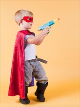 Studio shot, Portrait of boy (2-5 years) wearing cape and holding toy gun. Photo : Jessica Peterson