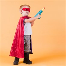 Studio shot, Portrait of boy (2-5 years) wearing cape and holding toy gun. Photo : Jessica Peterson