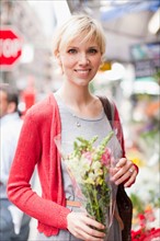 Portrait of smiling woman holding bunch of flowers. Photo : Jessica Peterson