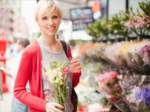 Portrait of smiling woman holding bunch of flowers outside of florist shop. Photo: Jessica Peterson