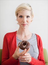Studio shot, Portrait of woman holding chocolate covered doughnut. Photo : Jessica Peterson
