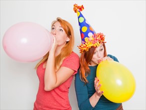 Studio Shot, Two young women blowing up pink and yellow balloons. Photo : Jessica Peterson