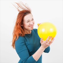Studio Shot, Portrait of woman holding yellow balloon and letting air out of it. Photo: Jessica