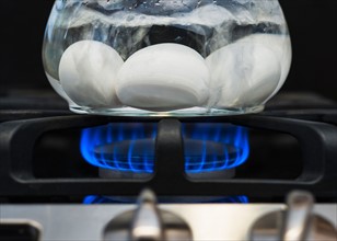 Close-up of eggs boiling on gas burner.