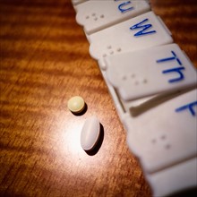 Pills and pill organizer on wooden table.