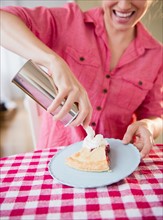 Young woman applying whipped cream on cherry pie