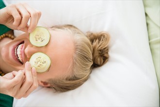 Young woman covering eyes with slices of cucumber