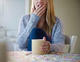 Young woman yawning over coffee mug