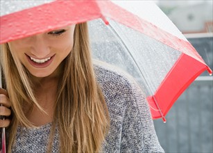 Smiling young woman with umbrella in rain