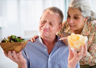 Elderly couple choosing between fresh salad and crisps