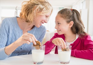 Mother and daughter (8-9 years) eating cookies with milk