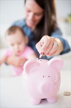 Mother with daughter (6-11 months) putting coins into piggybank