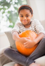 Portrait of smiling girl (6-7) sitting on sofa with pumpkin