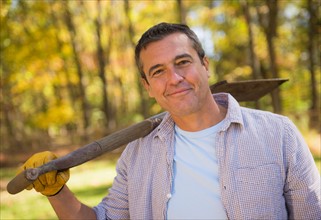 Portrait of smiling man holding shovel against his shoulder