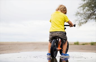 Toddler boy (2-3) riding bicycle in puddle