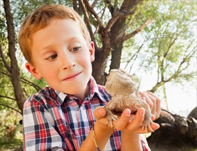 Little boy (6-7) looking curiously at a lizard that he is holding