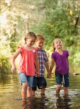Three kids (4-5, 6-7) holding hands and walking together in small stream
