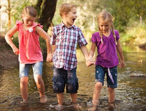 Three kids( 4-5, 6-7) holding hands and walking together in small stream