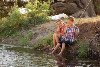Small boy and girl (6-7) fishing together with makeshift wooden stick in fishing poles in small stream