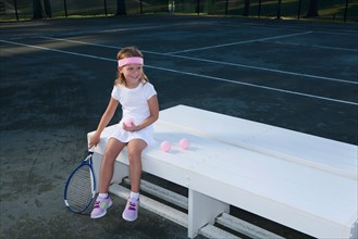 Girl sitting on bench and holding tennis racket