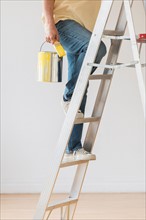 Man holding paint can and climbing ladder.