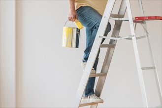 Man holding paint can and climbing ladder.