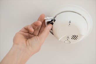 Hand changing battery in smoke alarm.