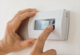 Hand changing settings on air conditioning thermostat.