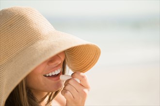 Woman wearing sun hat applying lipstick. Photo : Jamie Grill