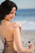 Woman applying suntan lotion at beach. Photo : Jamie Grill