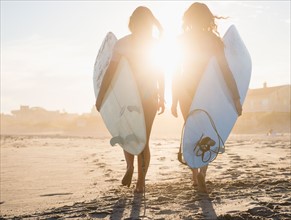 Two female surfers walking on beach at sunset. Photo : Jamie Grill