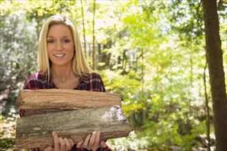 Portrait of woman holding logs in forest. Photo : Jamie Grill