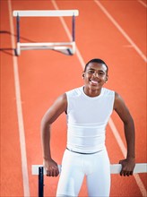 Portrait of smiling boy (12-13) leaning on hurdle on running track.