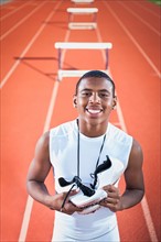 Portrait of smiling boy (12-13) leaning on hurdle on running track. Photo: Erik Isakson