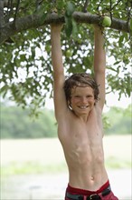 Boy (10-11) hanging on tree branch. Photo : pauline st.denis