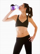 Young woman drinking water after exercising, studio shot. Photo : Mike Kemp