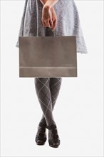 Low section of young woman holding shopping bag, studio shot. Photo: Mike Kemp
