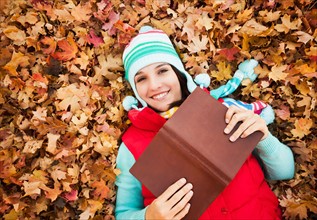 Portrait of young woman with book lying on autumn leaves . Photo : Mike Kemp