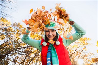 Portrait of smiling young woman throwing dry leaves in autumn forest. Photo: Mike Kemp