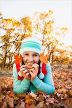 Portrait of smiling young woman lying on autumn leaves . Photo: Mike Kemp