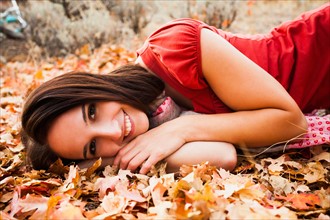 Portrait of smiling young woman lying on autumn leaves . Photo : Mike Kemp